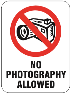 A sign featuring a red prohibitory circle and slash over a black and white camera icon, with the text 